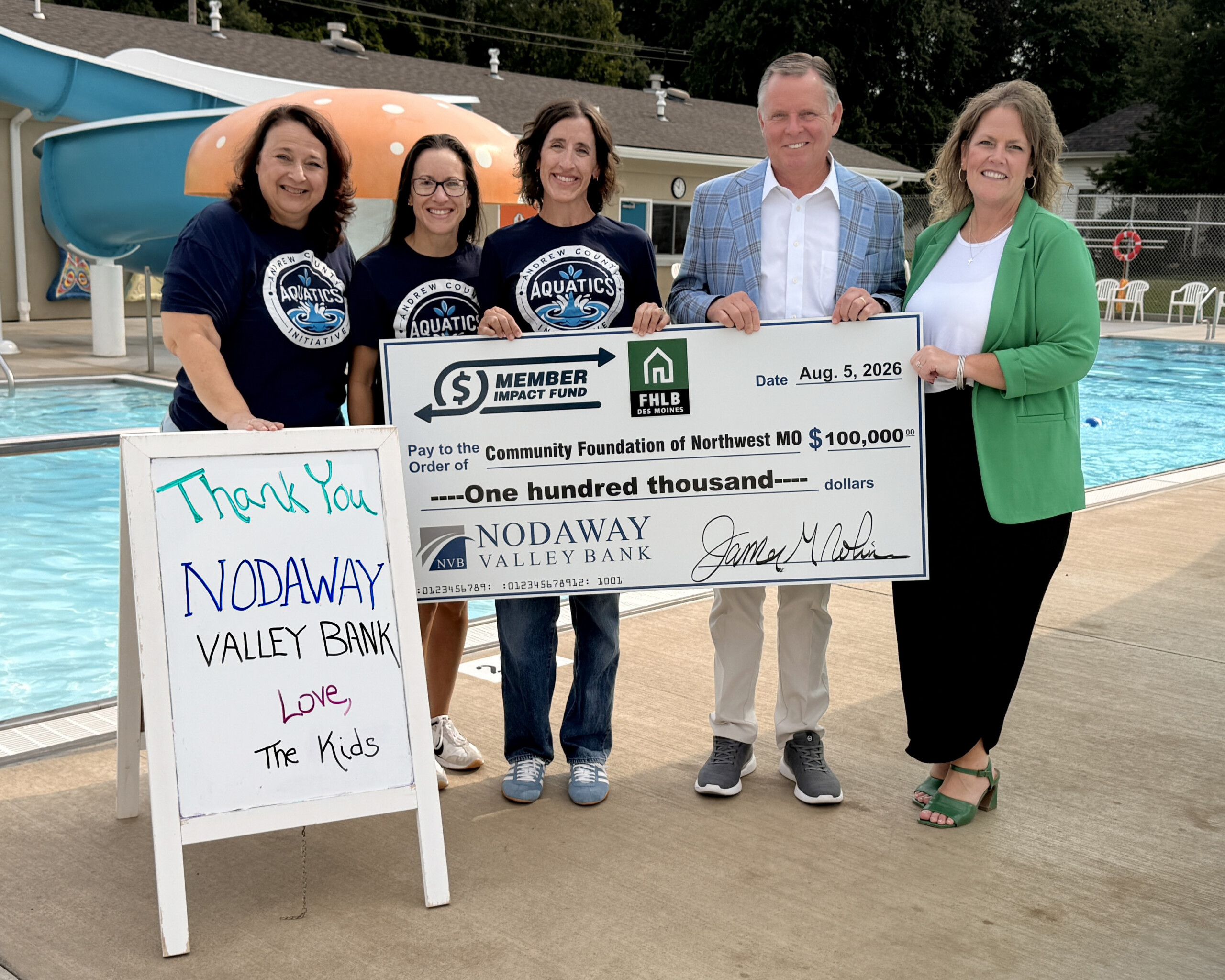 Andrew County Aquatics Initiative members and Nodaway Valley Bank representatives stand beside Savannah’s municipal pool holding a $100,000 Member Impact Fund donation check for the pool renovation project.