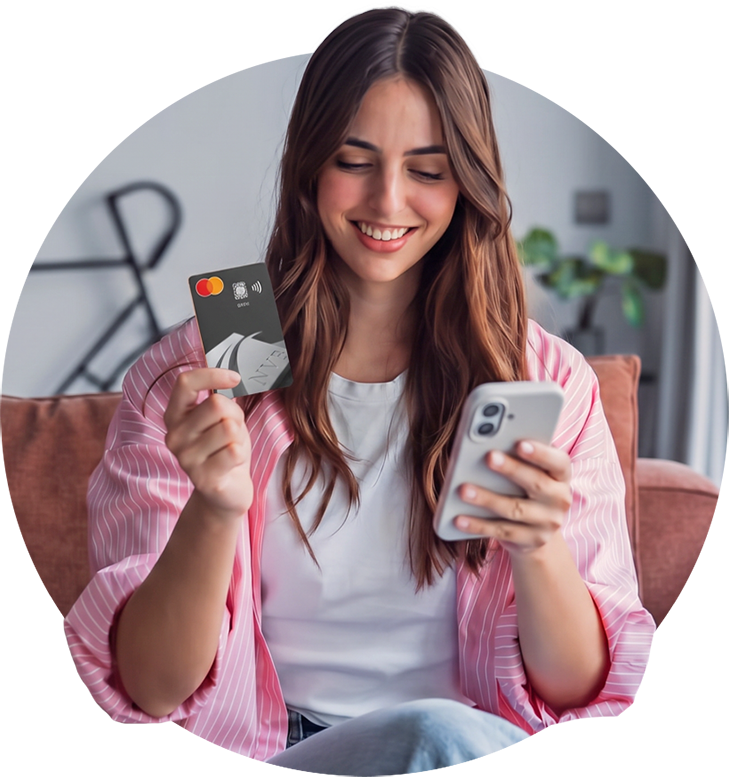 Smiling woman sitting on a couch, holding an NVB debit Mastercard in one hand and a smartphone in the other.